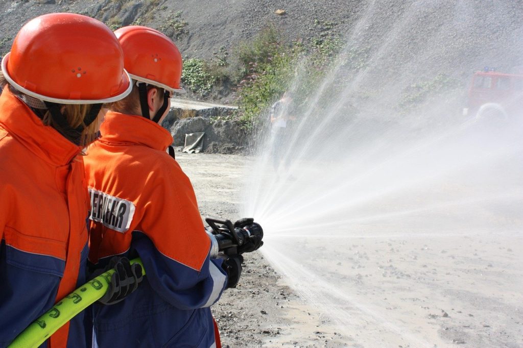 Zwei Jugendfeuerwehrleute, Rückansicht, mit einem Hohlstrahlrohr in der Hand, löschend