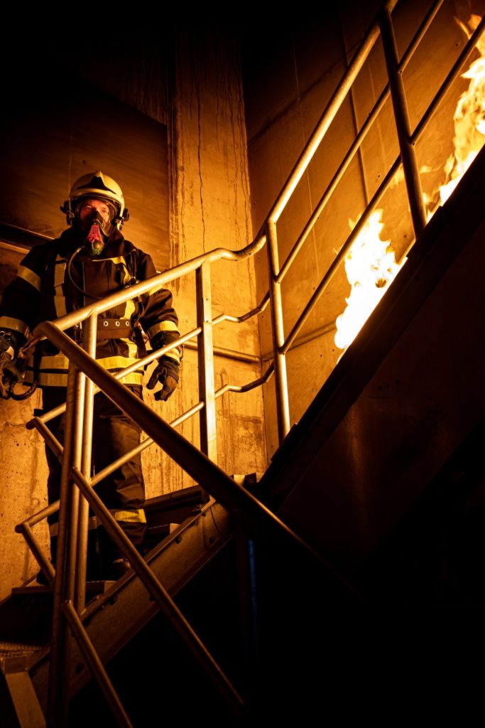 Feuerwehrmann steht auf einer Treppe, es brennt auf dem obersten Absatz