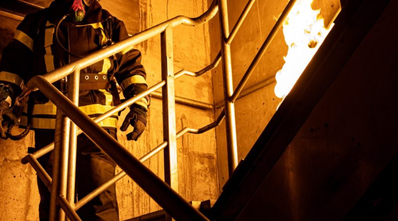 Feuerwehrmann steht auf einer Treppe, es brennt auf dem obersten Absatz