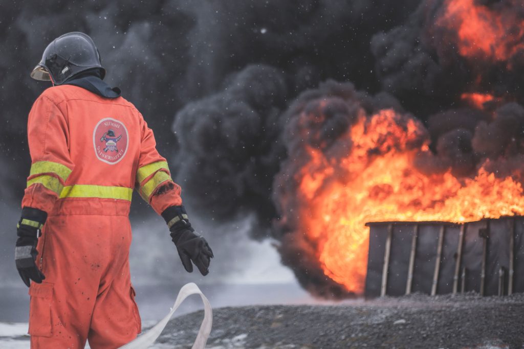 Feuerwehrmann, untätig, im Hintergrund ein Feuer mit dunklem Rauch